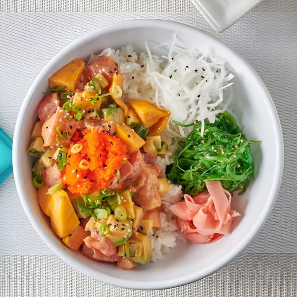 A colorful poke bowl with salmon, mango, avocado, roe, seaweed, pickled ginger, and rice.